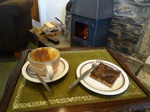 A capuccino and a traybake in front of a fireplace